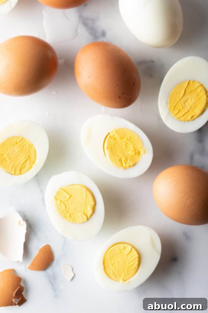 A beautifully arranged selection of a dozen hard-boiled eggs on a white marble surface, including whole eggs in shells, peeled white eggs, and egg halves revealing their rich, firm yolks.