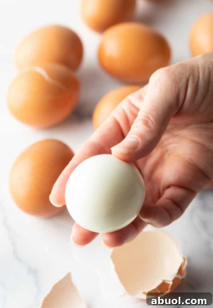 A hand gently holding a perfectly peeled hard-boiled egg against a soft, blurred background, highlighting its smooth, blemish-free surface.