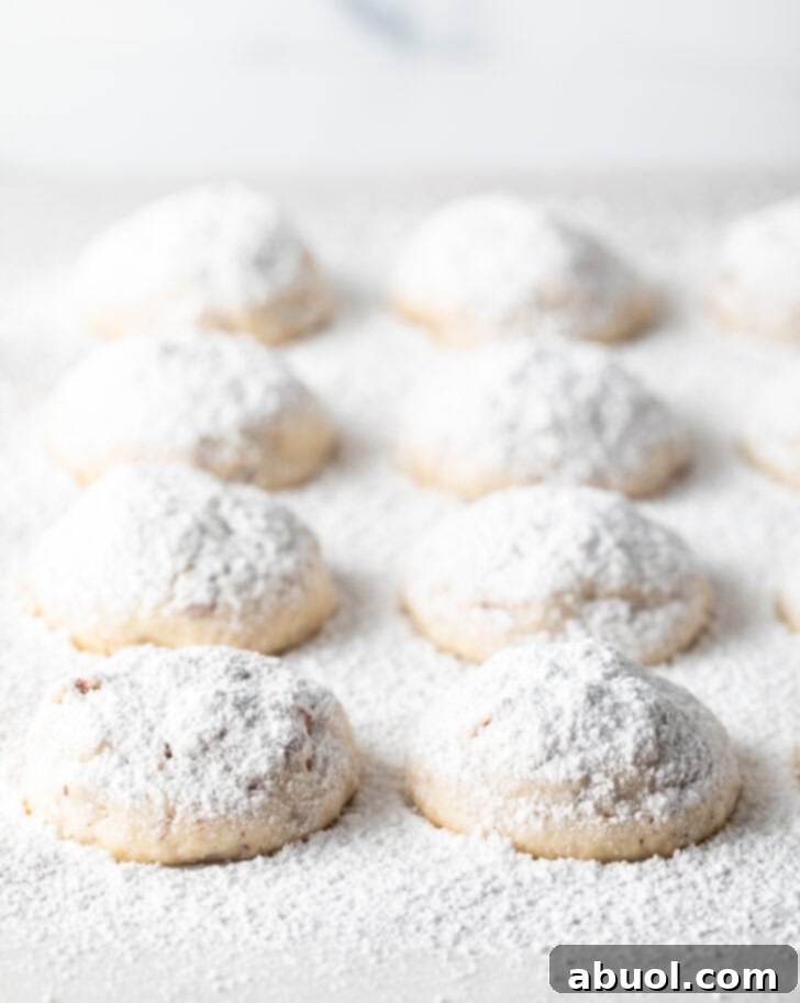 8 snowball cookies on a baking sheet, covered with a heavy layer of powdered sugar.