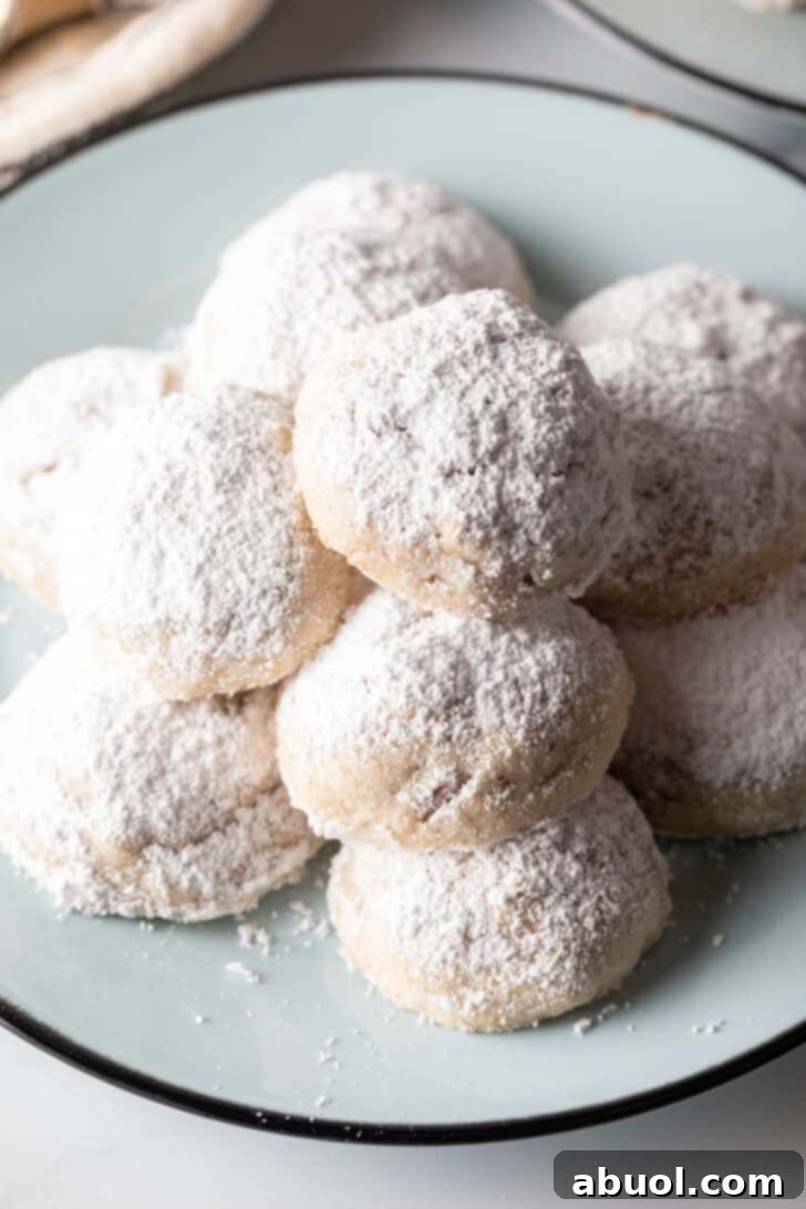 Light blue plate stacked with 3 layers of white Russian tea cakes covered in powdered sugar.