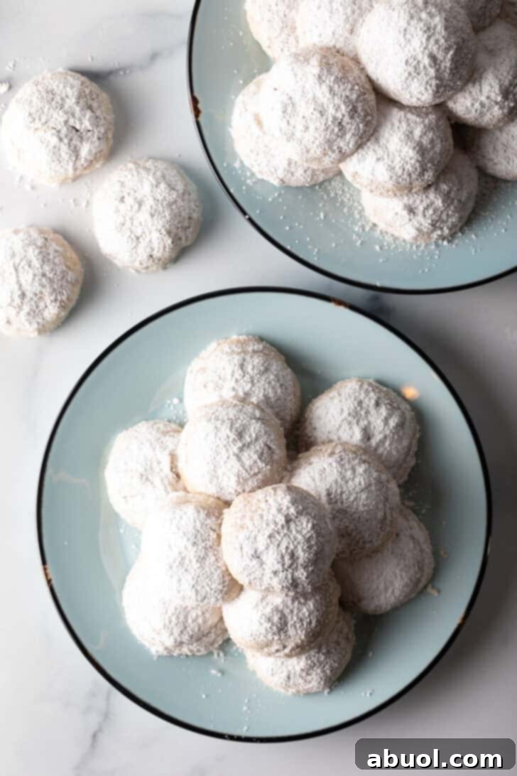 Light blue plate stacked with 3 layers of white Russian tea cakes covered in powdered sugar.