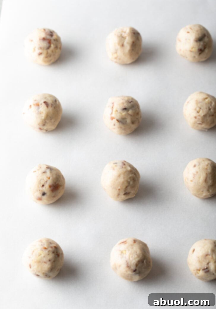 A dozen round balls of cookie dough on a baking sheet.