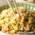 Chopsticks holding a bite of fried rice with crab, taking it from a plate of the rice.