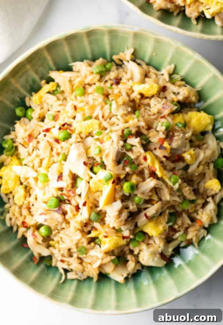 Fragrant Thai Crab Fried Rice 4 Top down view of a green plate with crab fried rice with chunks of crab meat and peas.