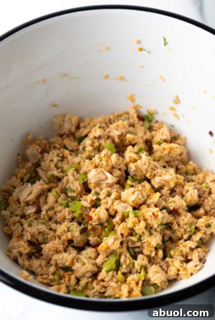 Inside a white mixing bowl, perfectly flaked salmon is thoroughly combined with breadcrumbs and fresh herbs, forming a uniform mixture ready for patty formation.