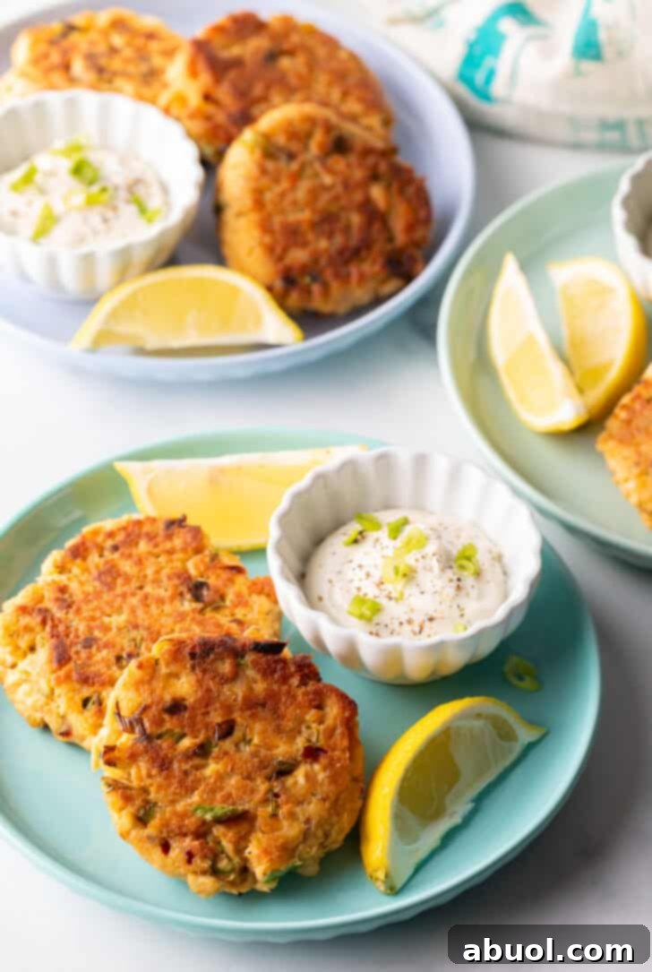 A classic old-fashioned salmon patties recipe presented on a green plate, accompanied by a white ramekin of tartar sauce and two fresh lemon wedges, showcasing the inviting golden hue of the patties.