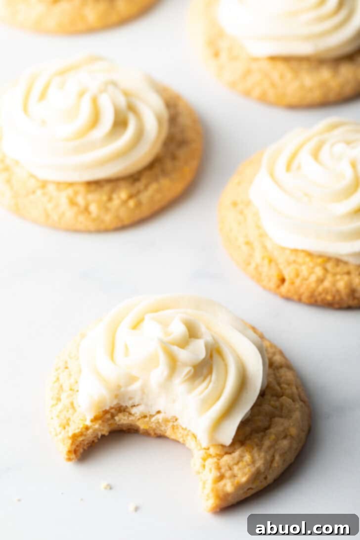 Several honey butter cornbread cookies on a white background, each topped with piped frosting. The cookie closest to camera has a bite taken out.
