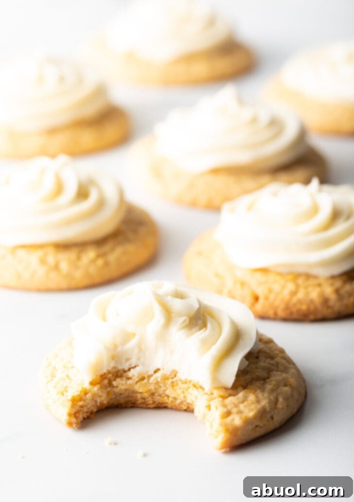 Several honey butter cornbread cookies on a white background, each topped with piped frosting. The cookie closest to camera has a bite taken out.