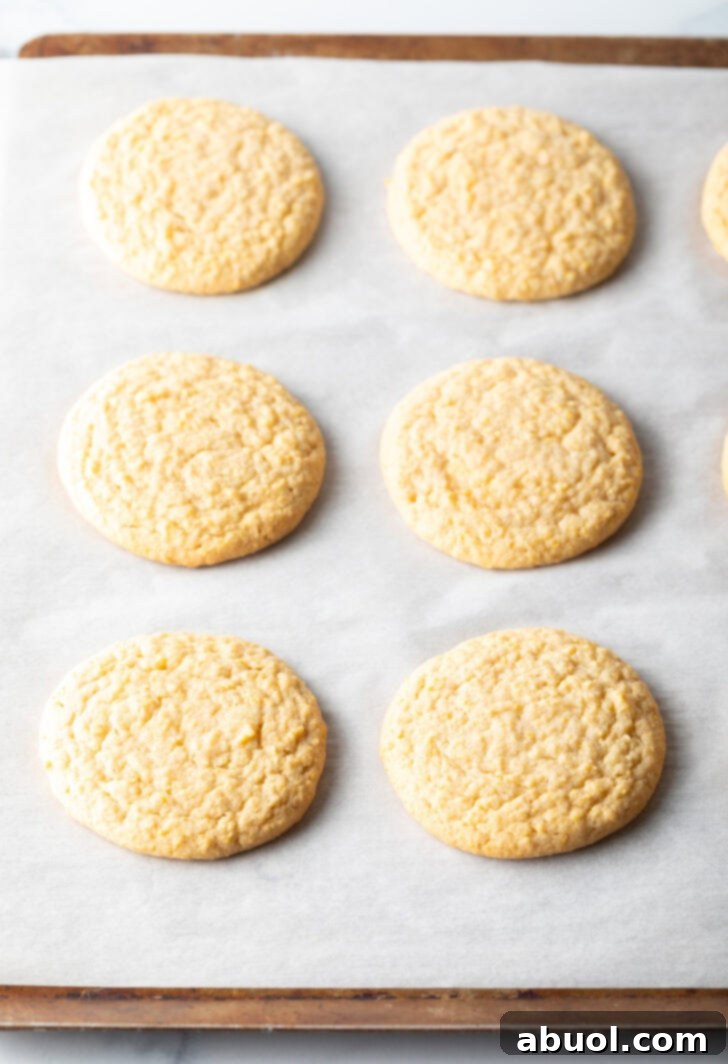 6 flat baked cornbread cookies on a baking sheet.