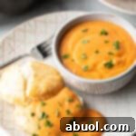 White plate with white bowl of red tomato gravy, next to a split open biscuit that's coated with the gravy and fresh chopped parsley.
