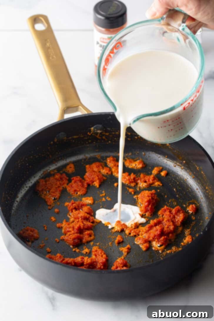 Pouring cream into a black skillet with tomato paste.