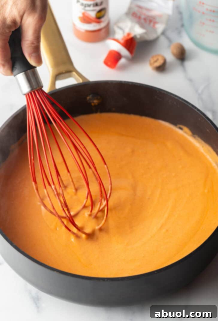 Deep black skillet with red gravy and a red whisk.