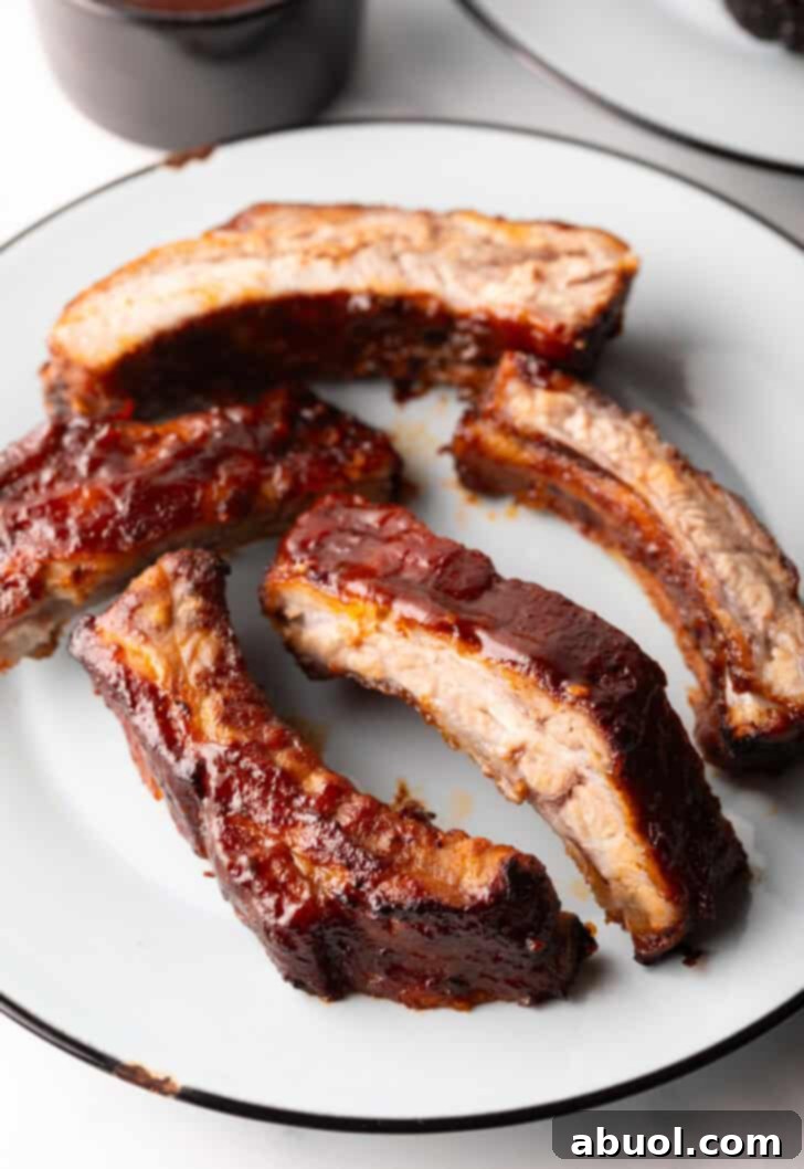 Five perfectly cooked air fried baby back ribs arranged on a white plate, glistening with barbecue sauce.