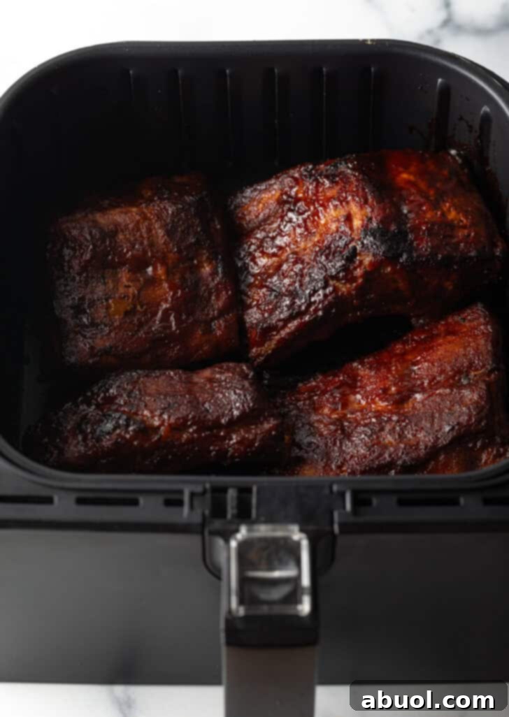 Finished baby back ribs coated in sticky BBQ sauce, nestled in an air fryer basket, ready to be served.