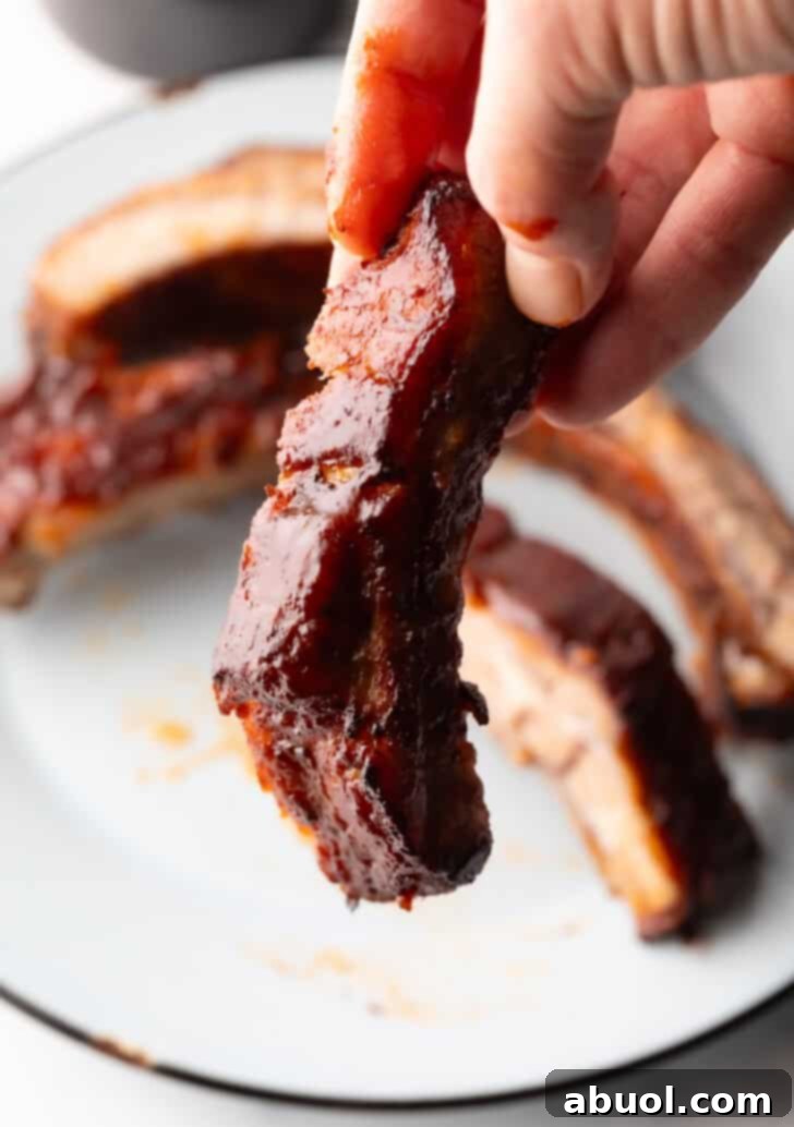 A hand holding a single, glazed barbecue rib up to the camera, showcasing its tender meat.