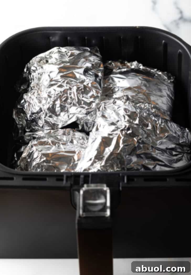 Ribs wrapped tightly in aluminum foil, cooking inside an air fryer basket, ensuring tender results.
