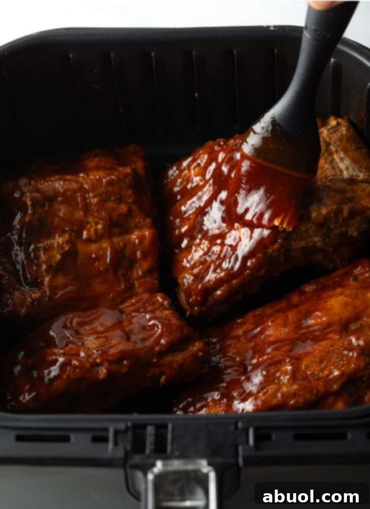 A hand basting air fried ribs with rich barbecue sauce inside the air fryer, creating a delicious glaze.