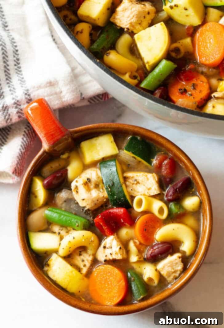 A top-down view of a large, handle-equipped mug, filled with steaming chicken minestrone soup, garnished with a sprig of rosemary.