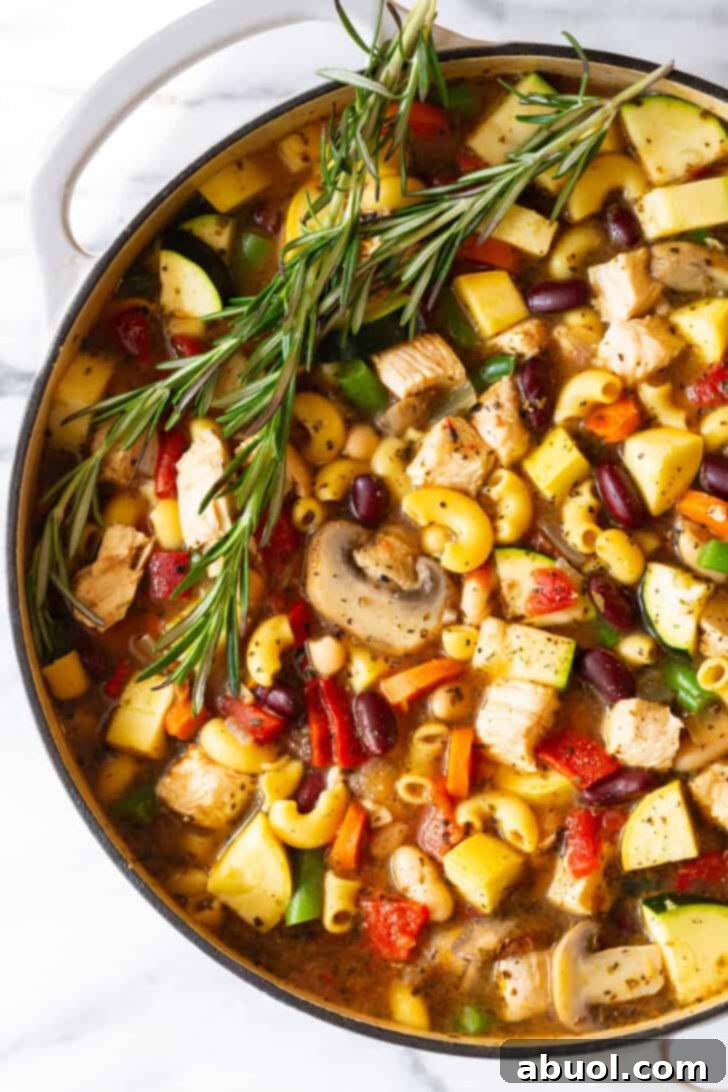 A white pot brimming with perfectly cooked chicken minestrone soup, garnished with fresh sprigs of rosemary, ready to be served.