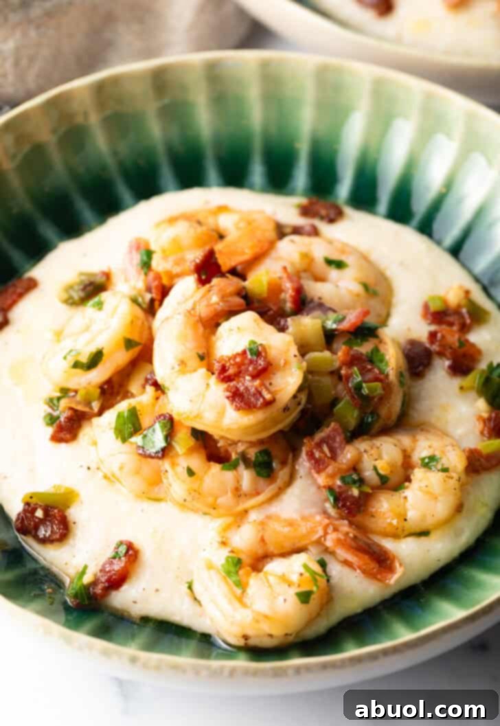 A vibrant green bowl brimming with creamy, cheesy grits, generously topped with perfectly cooked Cajun shrimp and crumbled, crispy bacon. This visually appealing dish showcases the rich textures and colors of a classic Southern favorite, inviting you to savor every bite.
