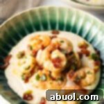 A green bowl filled with rich, cheesy grits, topped generously with succulent Cajun shrimp and crispy crumbled bacon, a perfect depiction of this beloved Southern dish.