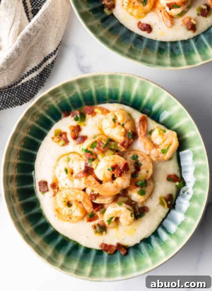 A close-up view of a green bowl filled with creamy, cheesy grits, topped with perfectly seasoned Cajun shrimp and crumbled bacon. The focus highlights the luscious texture of the grits and the vibrant colors of the toppings, making it irresistibly appetizing.
