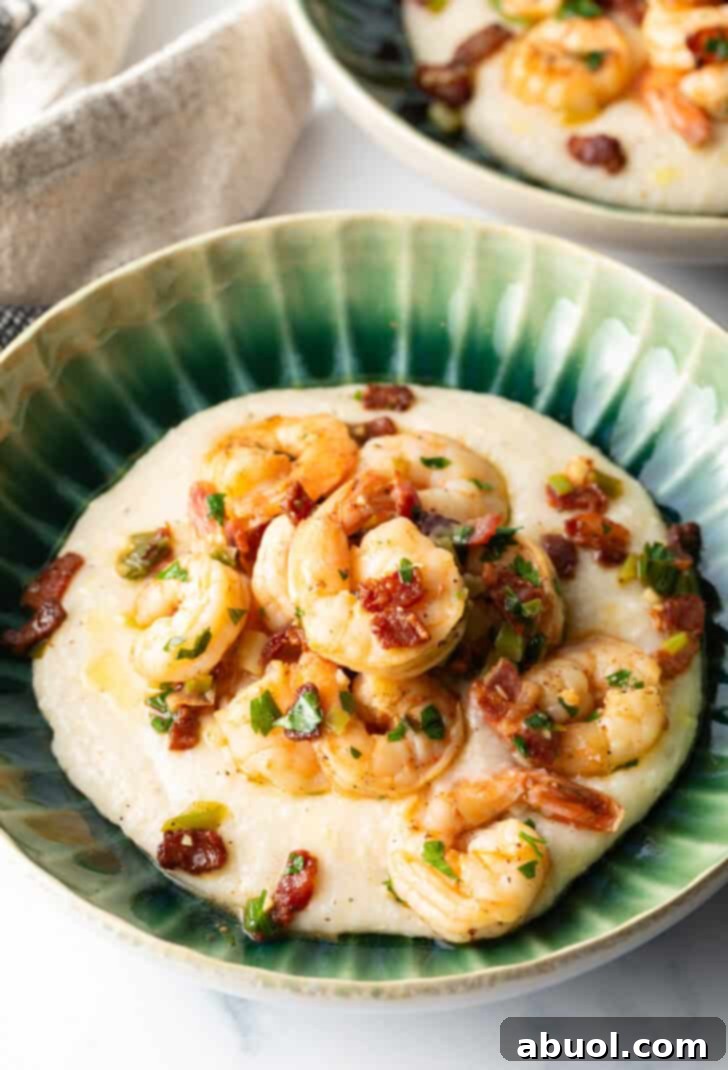 A vibrant bowl of cheesy grits crowned with seasoned Cajun shrimp and crispy bacon, garnished with fresh green onions. This inviting presentation captures the essence of a classic Southern comfort meal, ready to be enjoyed.