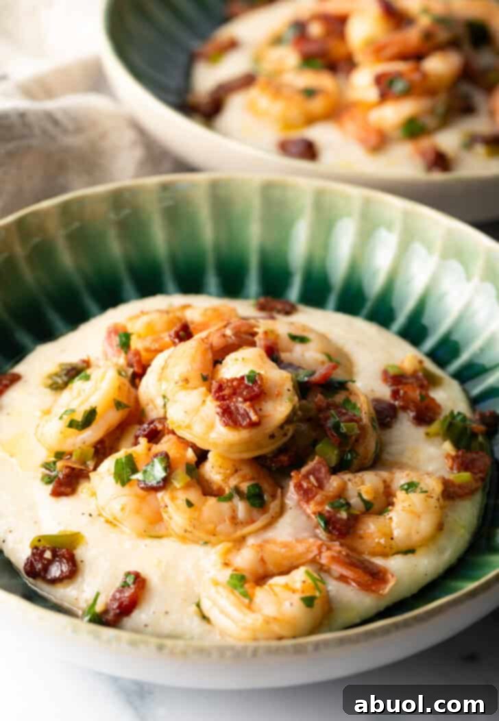 A beautifully presented green bowl filled with creamy, cheesy grits, topped with perfectly cooked Cajun shrimp and crispy bacon. The appetizing display promises a delightful culinary experience.