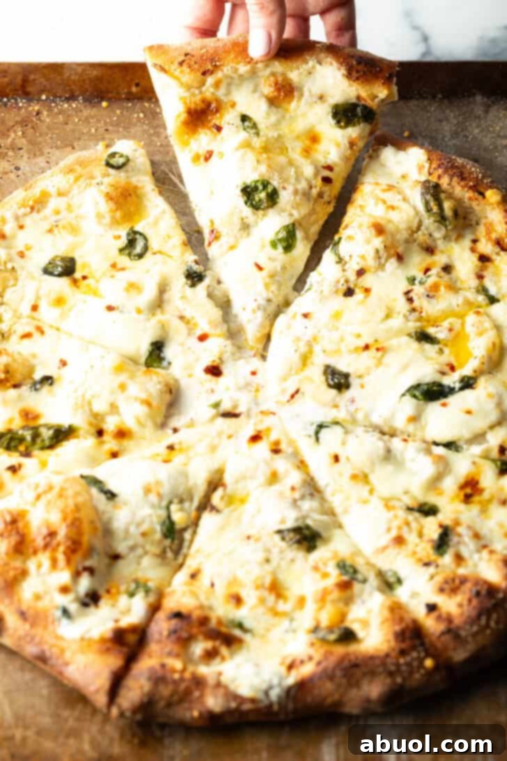 Pizza with white sauce cut into 8 slices. A hand is removing one slice of pizza.