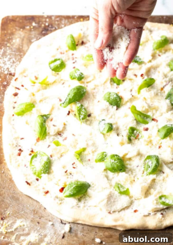 Hand adding shredded cheese on top of the unbaked pizza.
