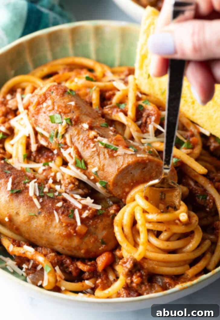 Hand swirling pasta onto a fork from a green bowl of spaghetti and sausage pasta.