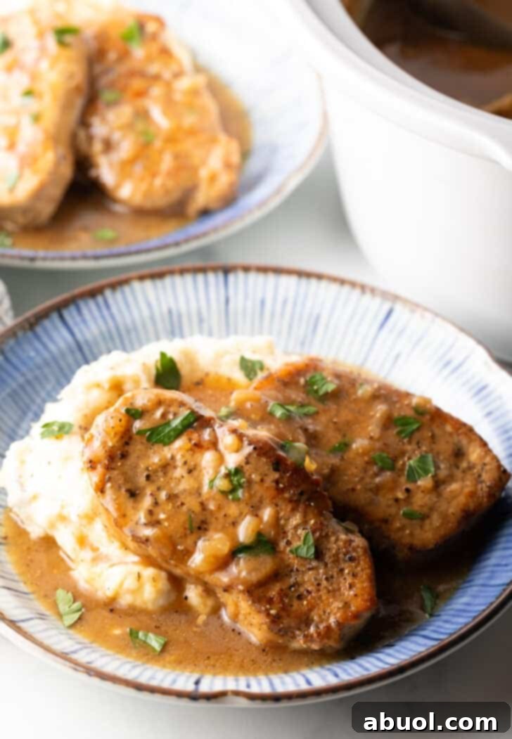 Two boneless pork chops on a plate of mashed potatoes and brown onion gravy.