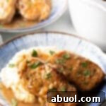 Two boneless pork chops on a plate of mashed potatoes and brown onion gravy.