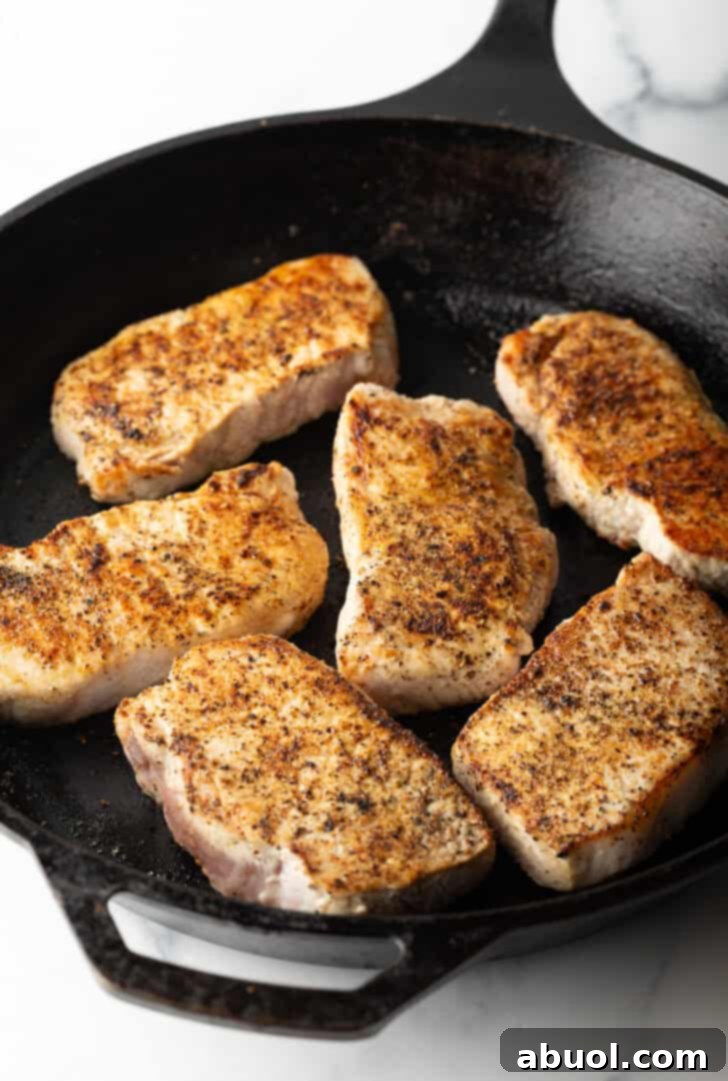 6 boneless pork chops searing in a cast iron skillet.