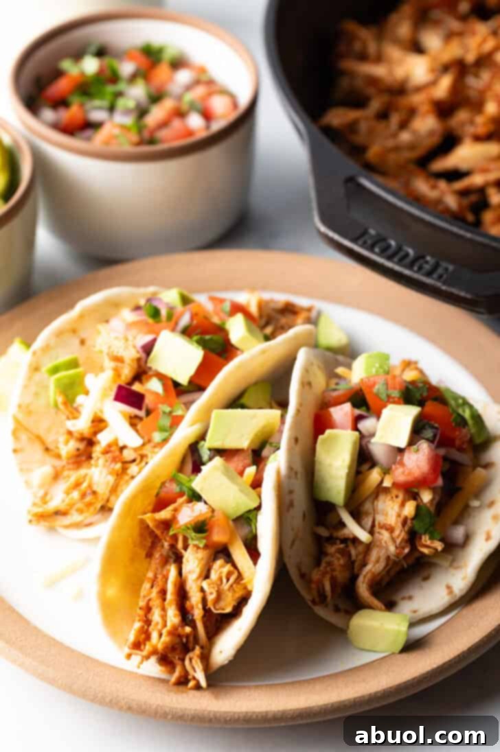 Three chicken tacos with chopped avocado on a plate together.