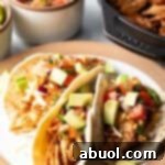 Three chicken tacos with chopped avocado on a plate together.