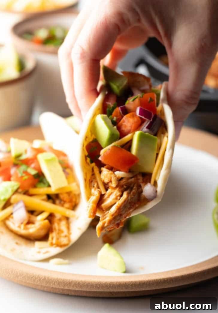 Hand picking up a taco with chicken, salsa, and chopped avocado.