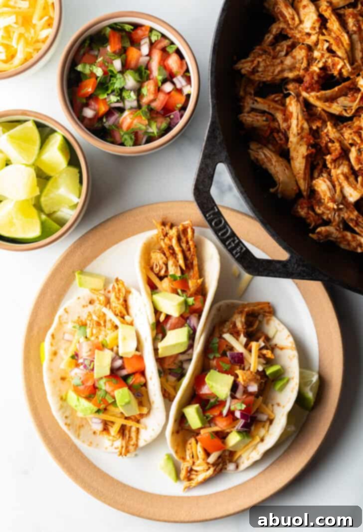 Three chicken tacos with chopped avocado on a plate together.