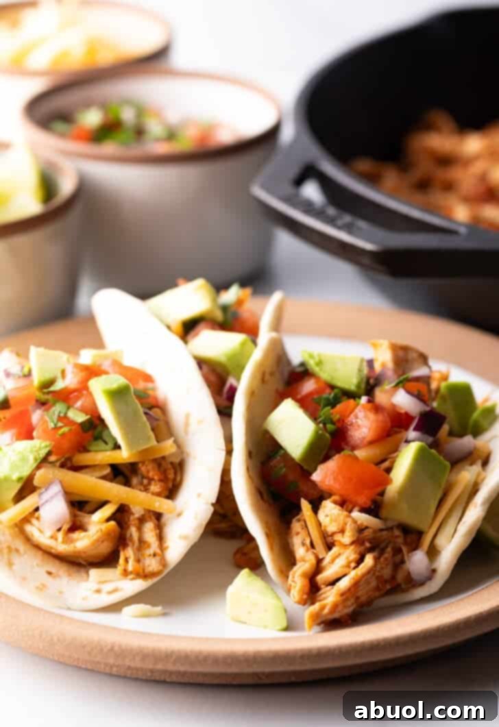 Three chicken tacos with chopped avocado on a plate together.