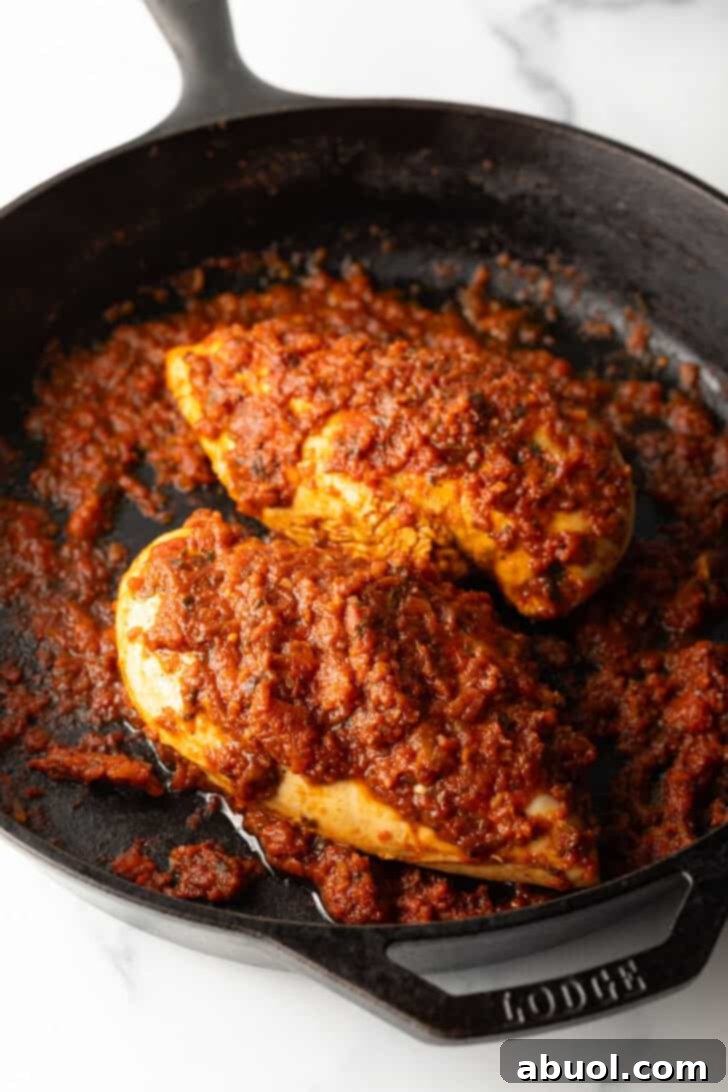 Two chicken breasts in a cast iron skillet with tomato sauce.