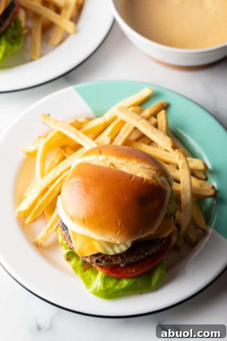 A juicy burger with melted cheese, fresh lettuce, and tomato on a bun, served on a plate with a side of crispy french fries.