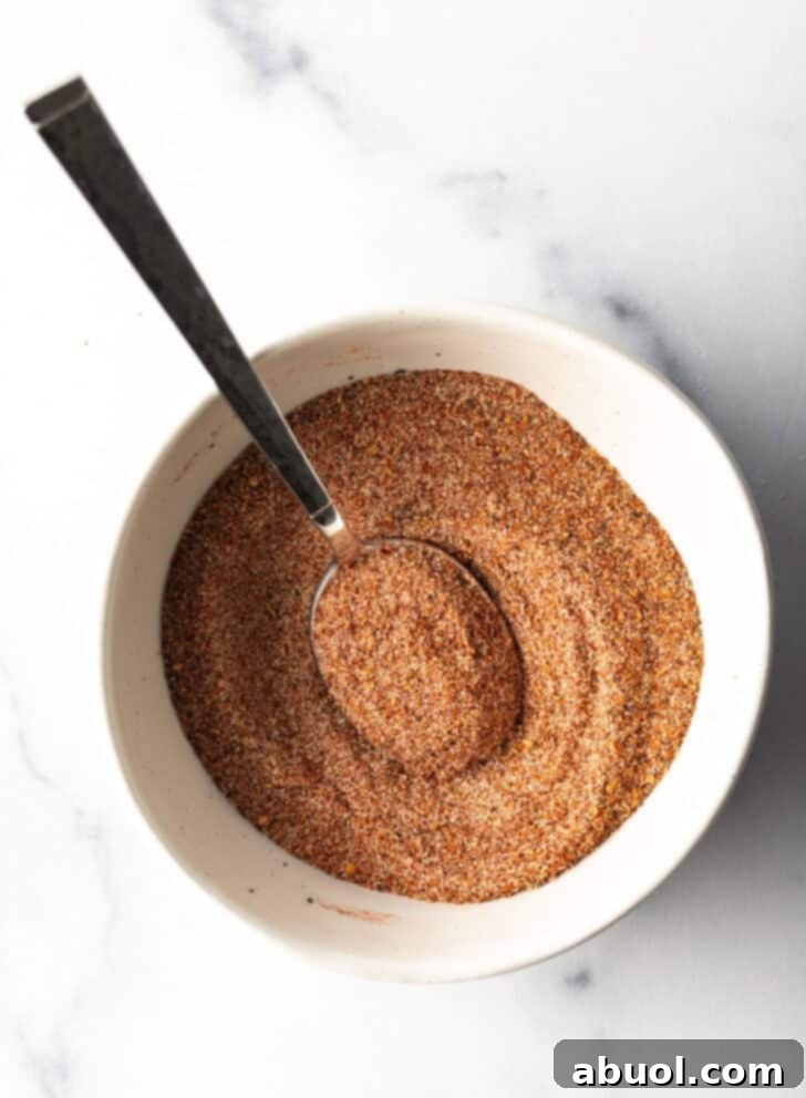 A top-down view of a white bowl filled with the vibrant blend of burger seasoning, with a spoon nestled within the spices.