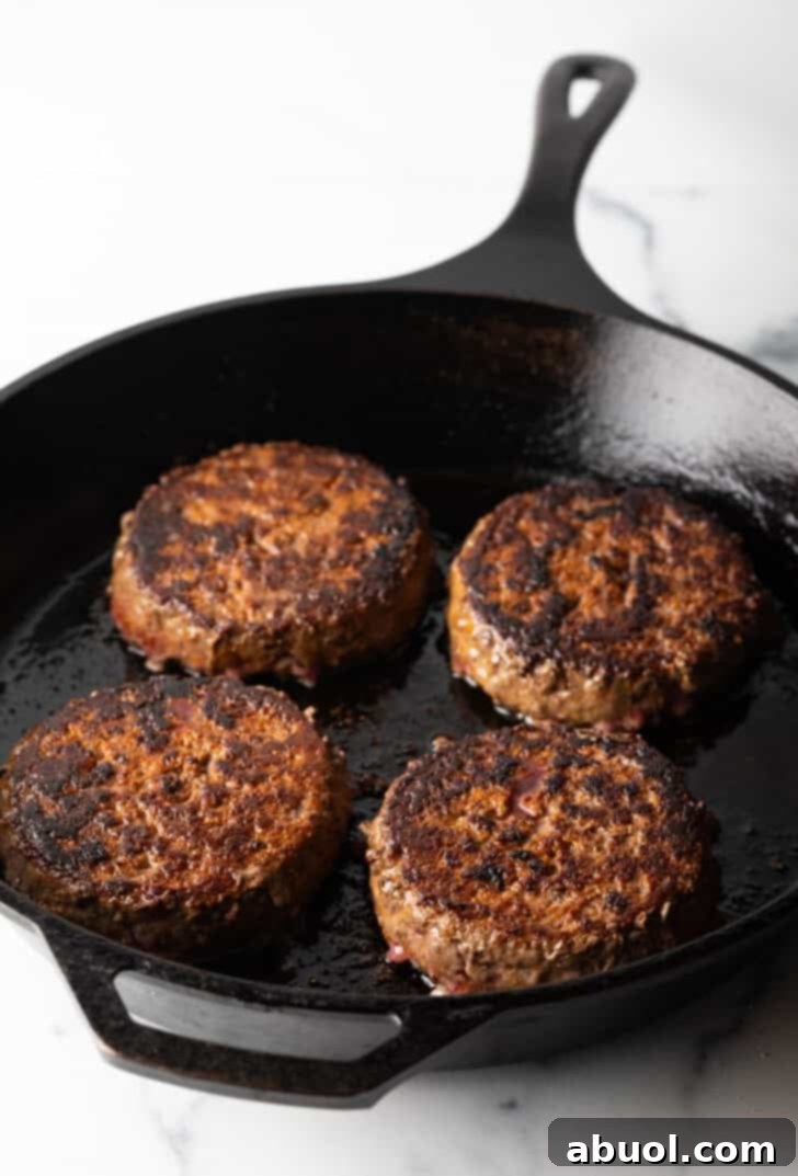 Four perfectly cooked, golden-brown hamburgers sizzling in a cast iron skillet, ready to be topped.