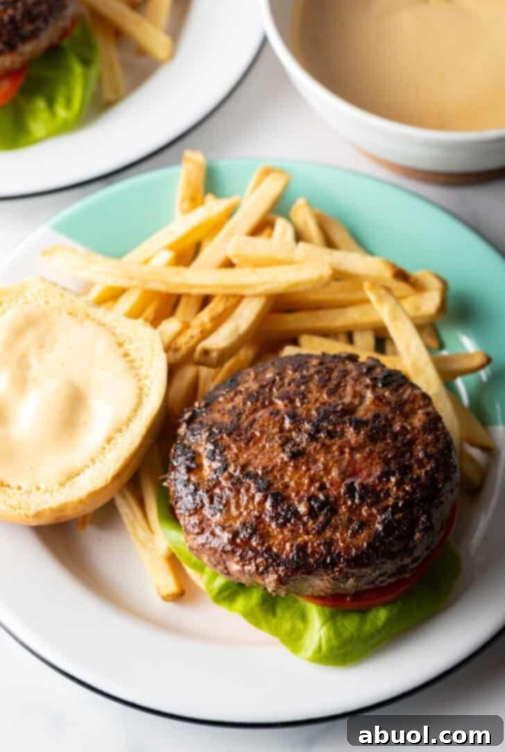 An open-faced burger showcasing its juicy patty, melted cheese, and fresh toppings, served on a plate next to a generous portion of golden fries.