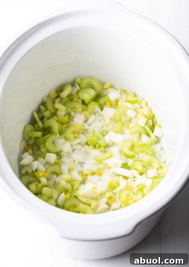 Chopped celery and onion in a white slow cooker.