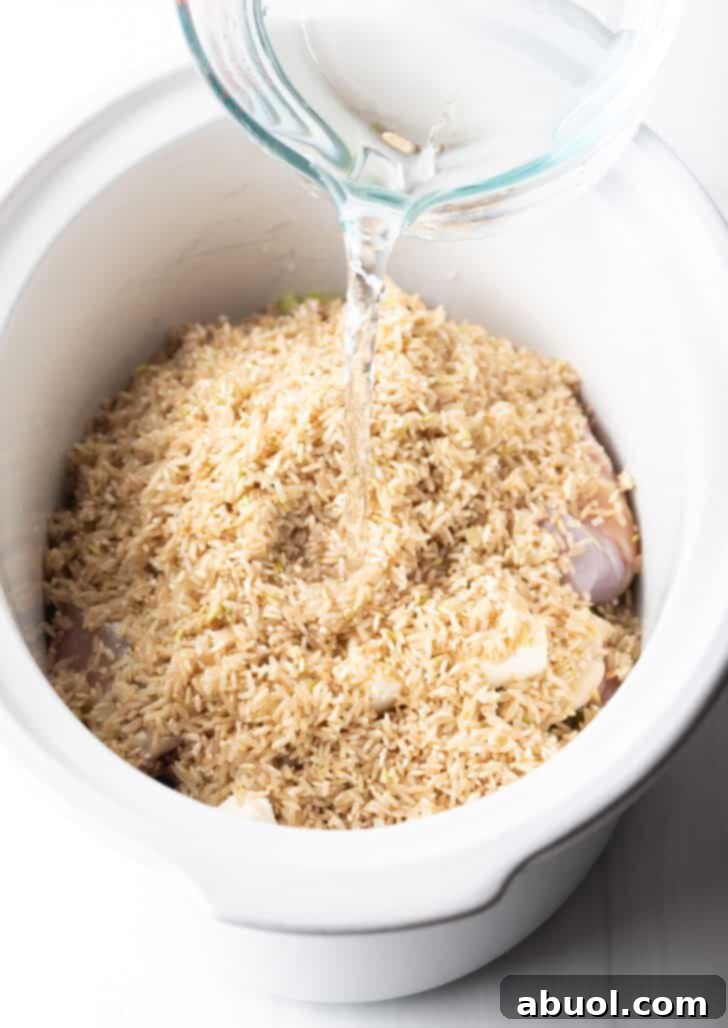 Adding water to a slow cooker with chicken thighs and brown rice.