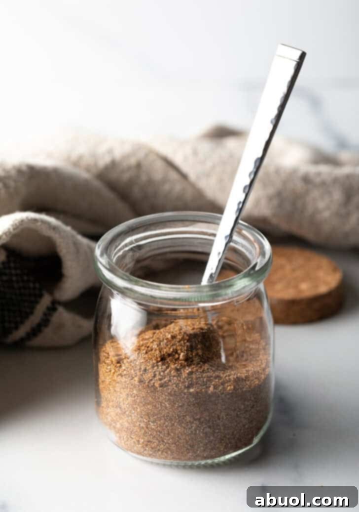 Small glass jar with pork chop seasoning and a metal spoon.