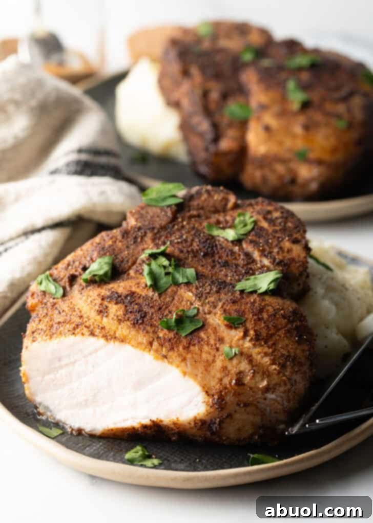 Browned seasoned bone-in pork chop on a plate with mashed potatoes, garnished with chopped parsley. The front piece of the chop has been cut off to show the juice meat inside.
