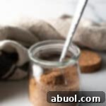 Small glass jar with pork chop seasoning and a metal spoon.