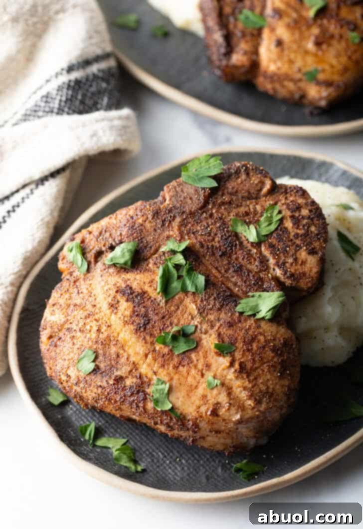 Browned seasoned bone-in pork chop on a plate with mashed potatoes, garnished with chopped parsley.